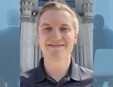 Portrait of a smiling young man with short blond hair, standing in front of a stone building.