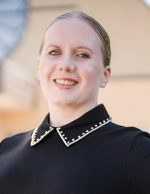 Smiling woman in a black top with pearl-trimmed collar, outdoors, head-and-shoulders pose.